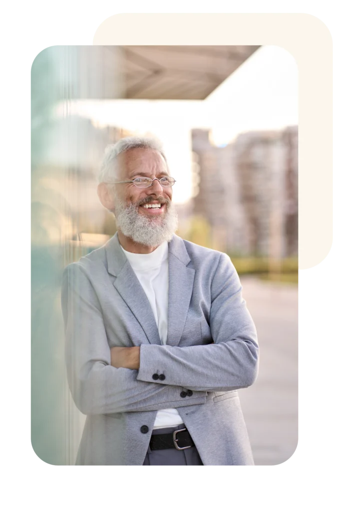 Smiling Mature Man Leans Against Glass Wall – Waypoint Family Business Advisory